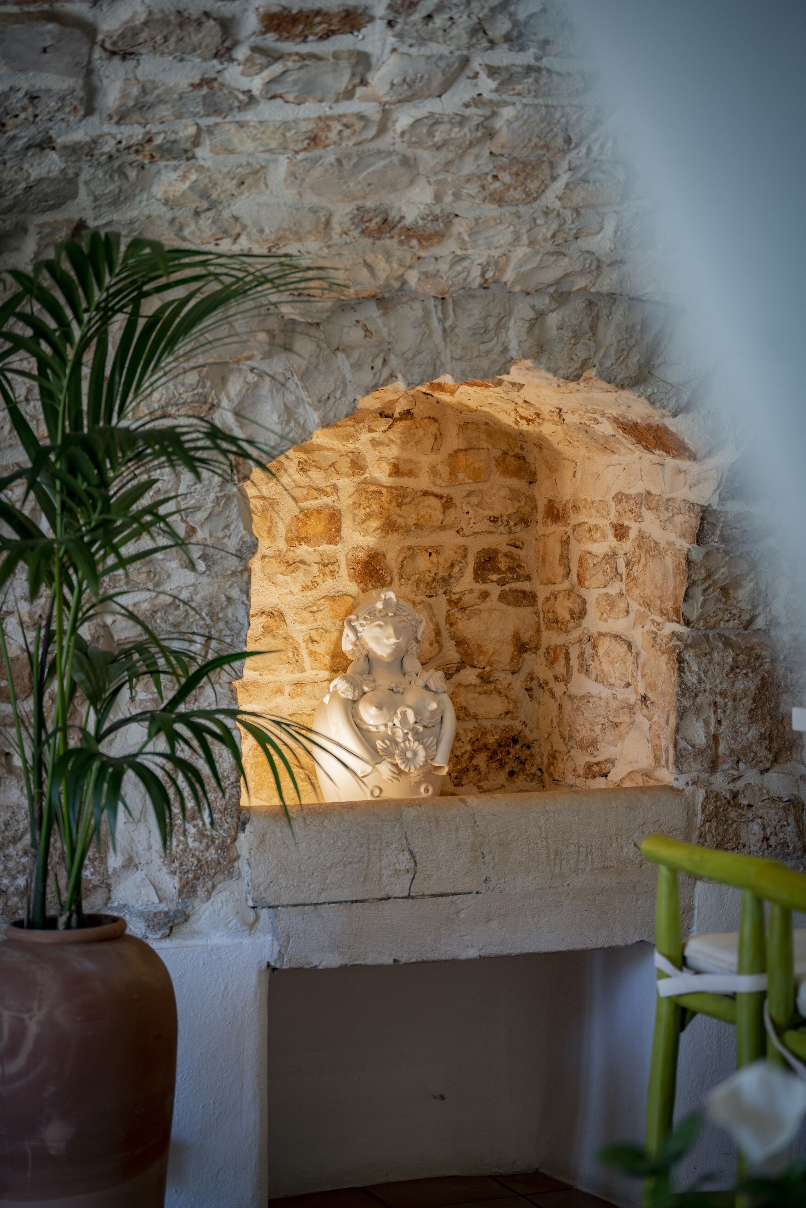 A stone fireplace with a statue, a potted plant, and a chair.