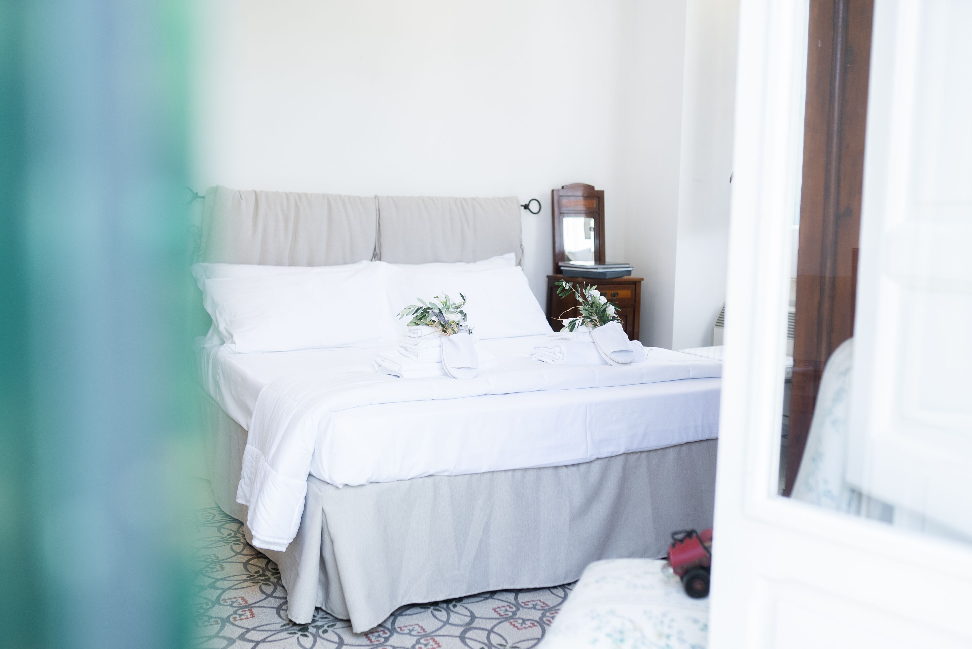 Una cama bien hecha con ropa de cama blanca, una mesita de noche con espejo y una pequeña planta en maceta.