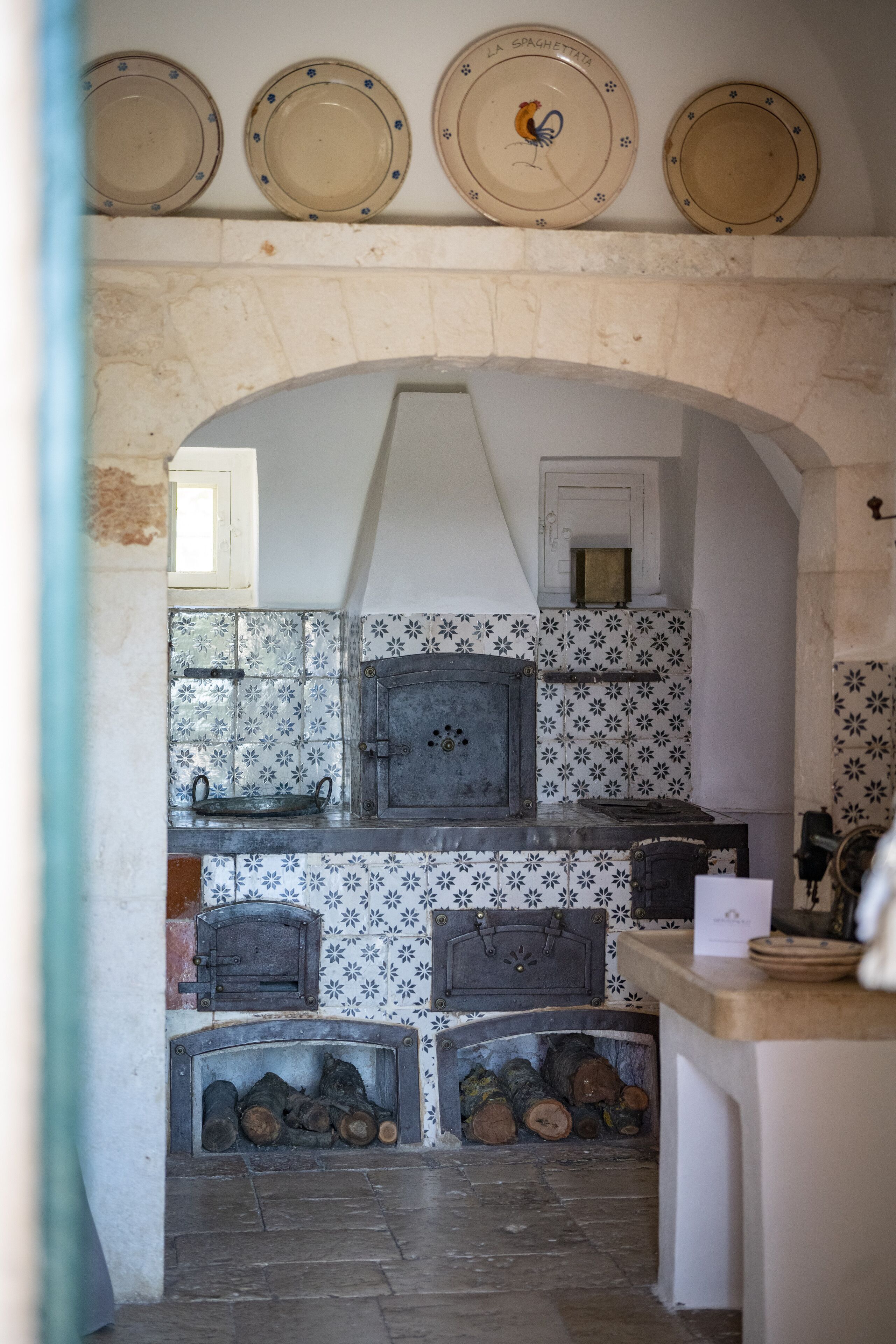 A rustic kitchen with a stone archway, tiled backsplash, and a wood-fired oven.
