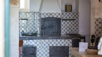 A rustic kitchen with a stone archway, tiled backsplash, and a wood-fired oven.