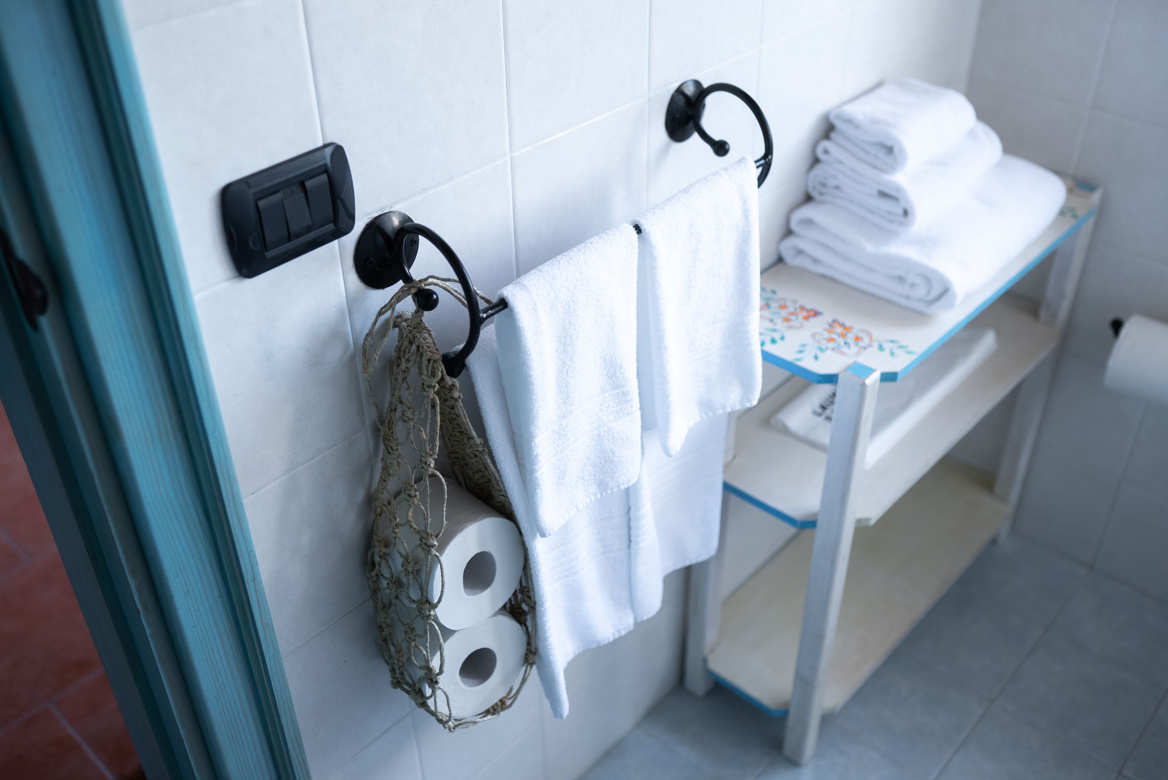 Kylpyhuoneessa on pyyheteline, jossa on pyyhe ja rulla WC-paperia, pieni pöytä, jonka päällä on taiteltuja pyyhkeitä, sekä ovi, jossa on kahva.