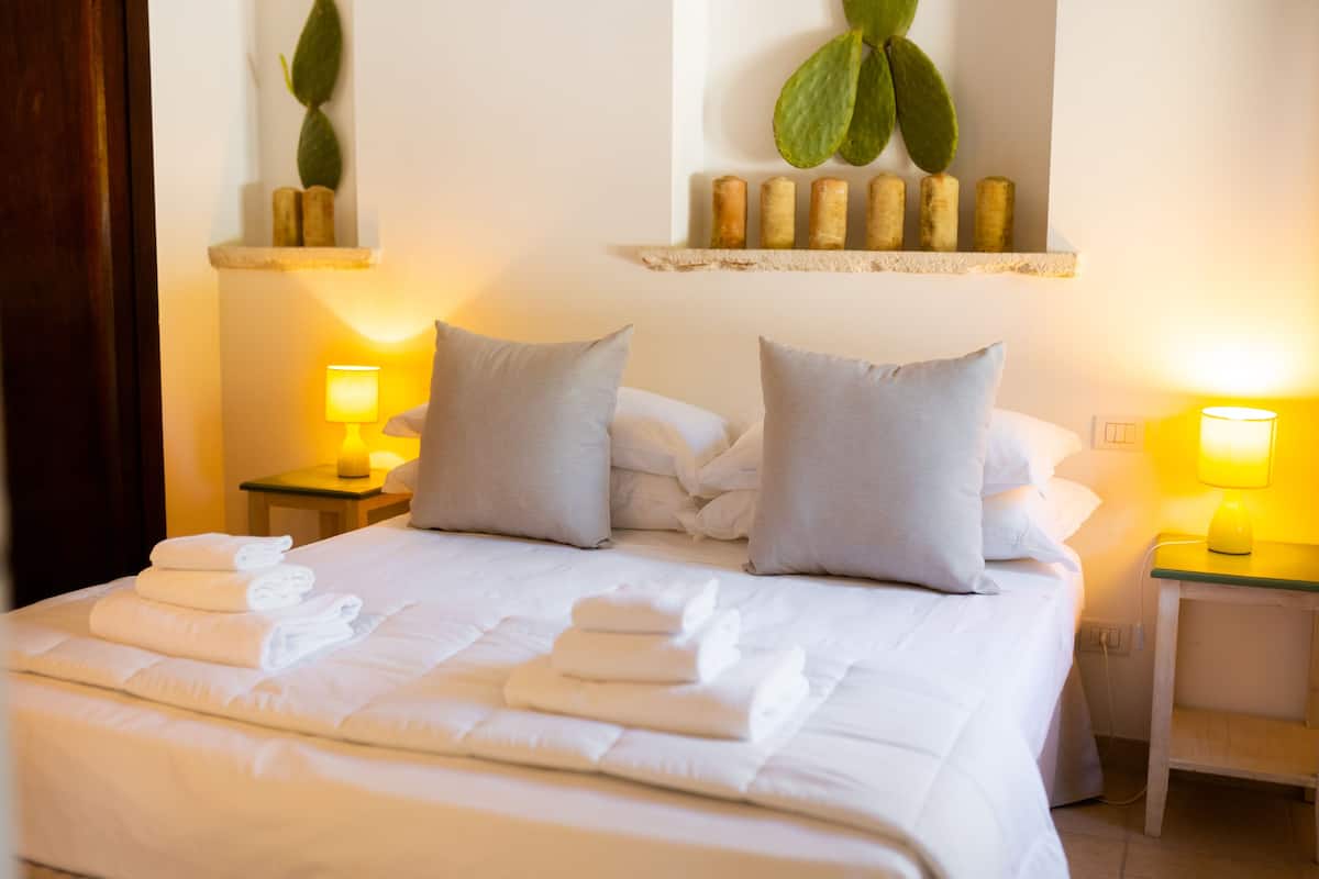 A neatly made bed with folded towels, two bedside tables with lamps, and decorative plants on the wall.