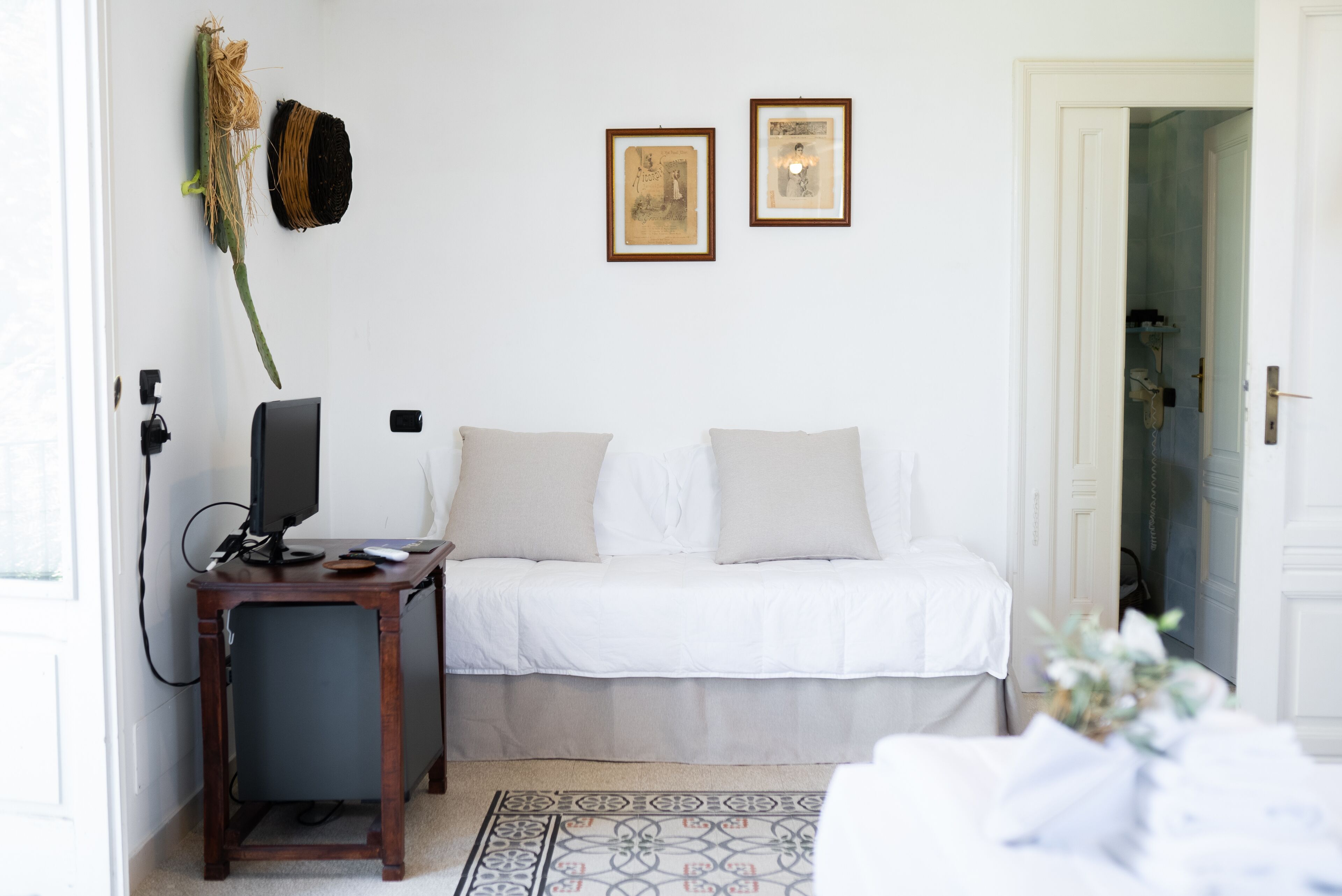 A bedroom with a bed, a desk with a computer, and two framed pictures on the wall.