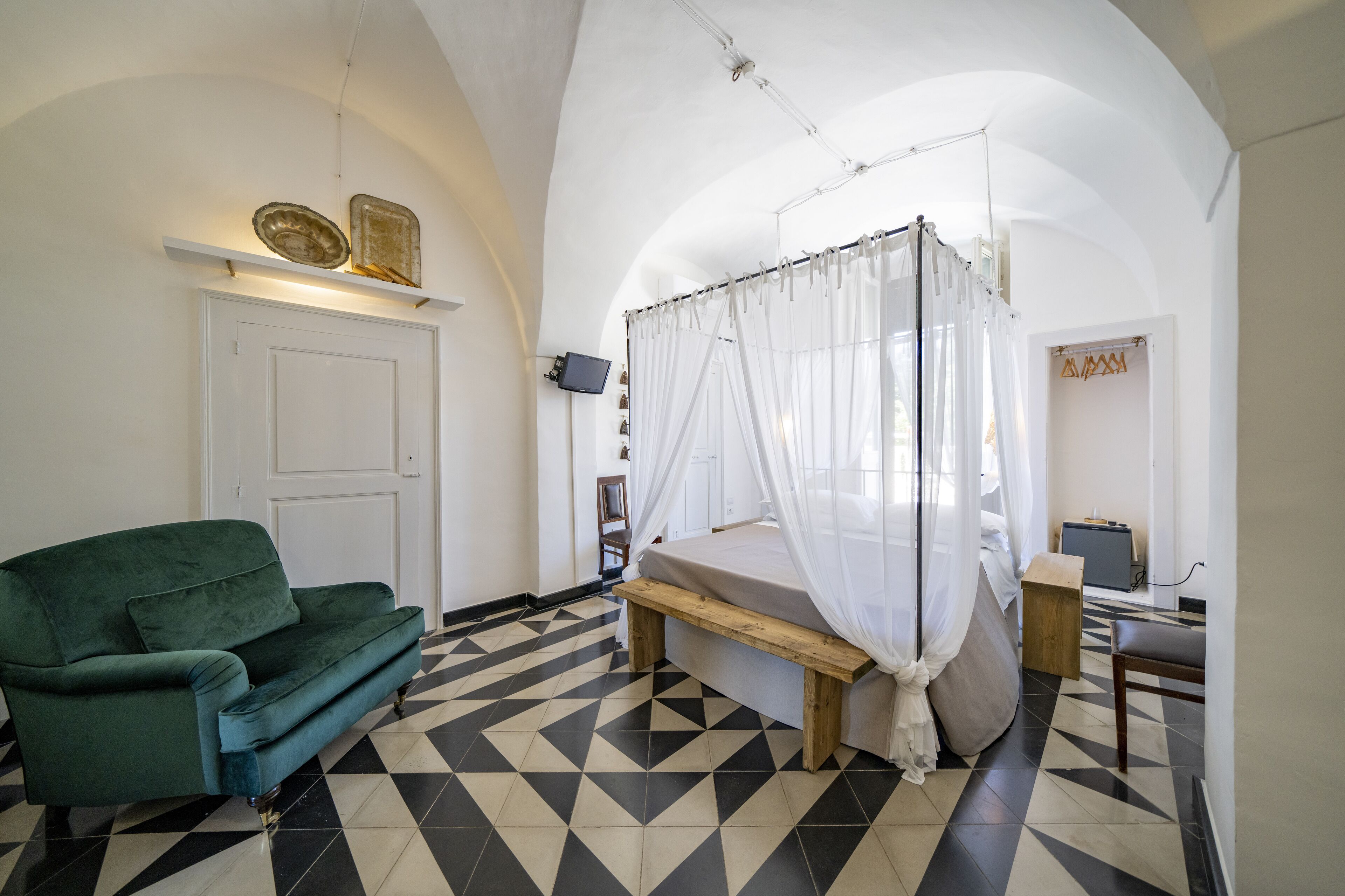 Un dormitorio con cama con dosel, un sofá verde, un televisor y suelo de baldosas.