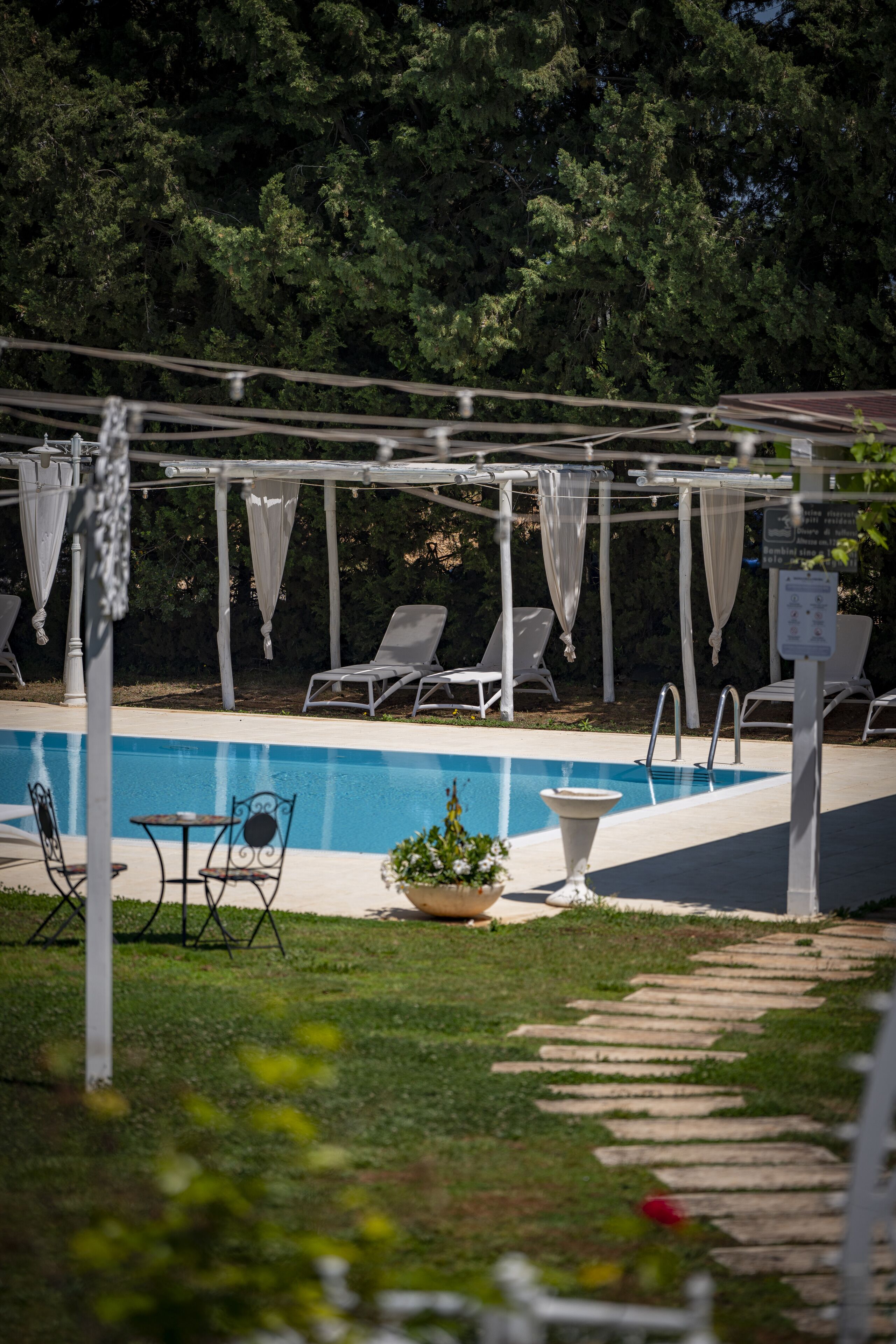 A pool area with lounge chairs and a pergola with white drapes.