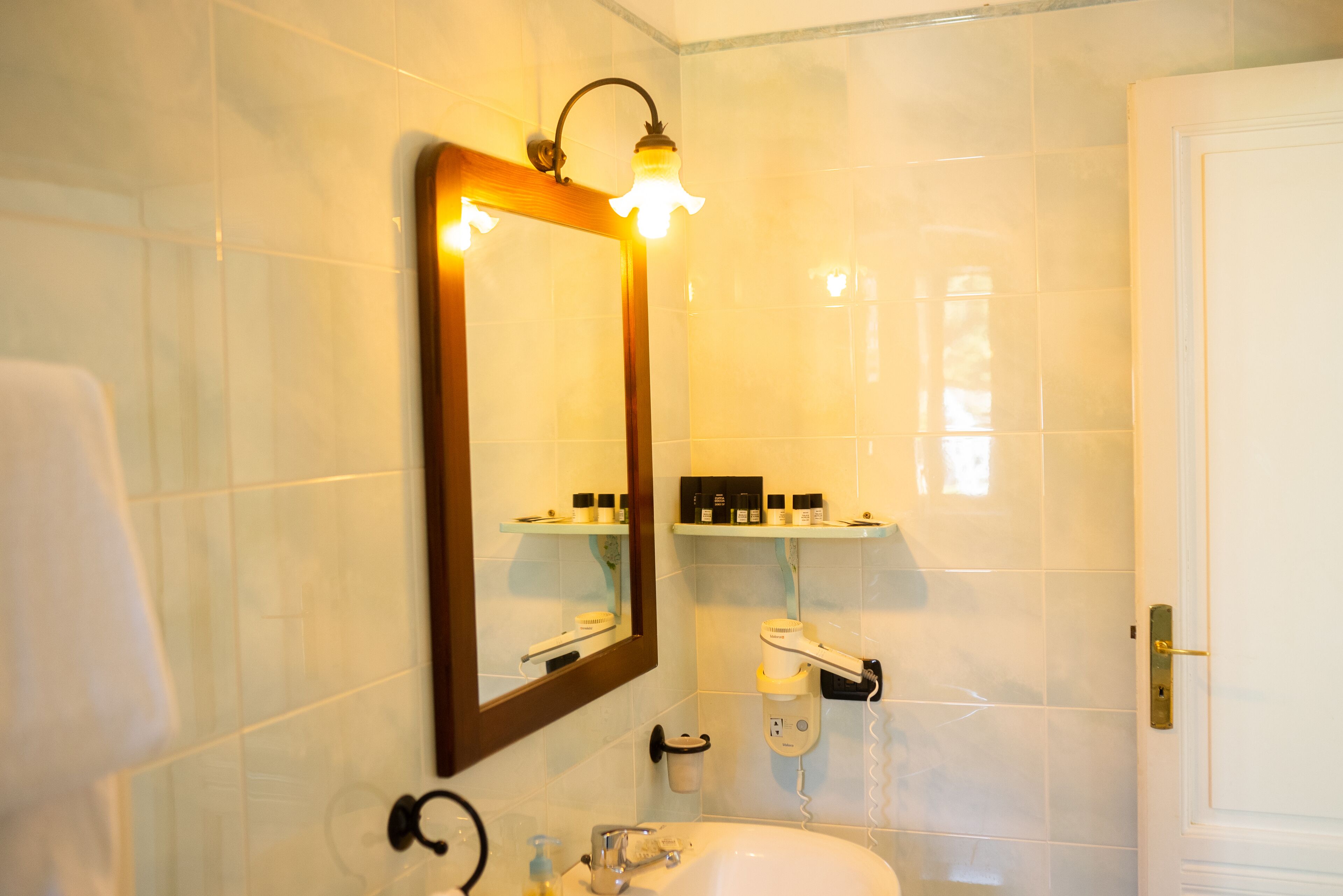 Un baño con un espejo grande, un lavabo, un perchero para toallas y estantes con artículos de aseo.