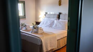 A neatly made bed with white linens and a quilt, a bedside table with a lamp, and a window with a green frame.