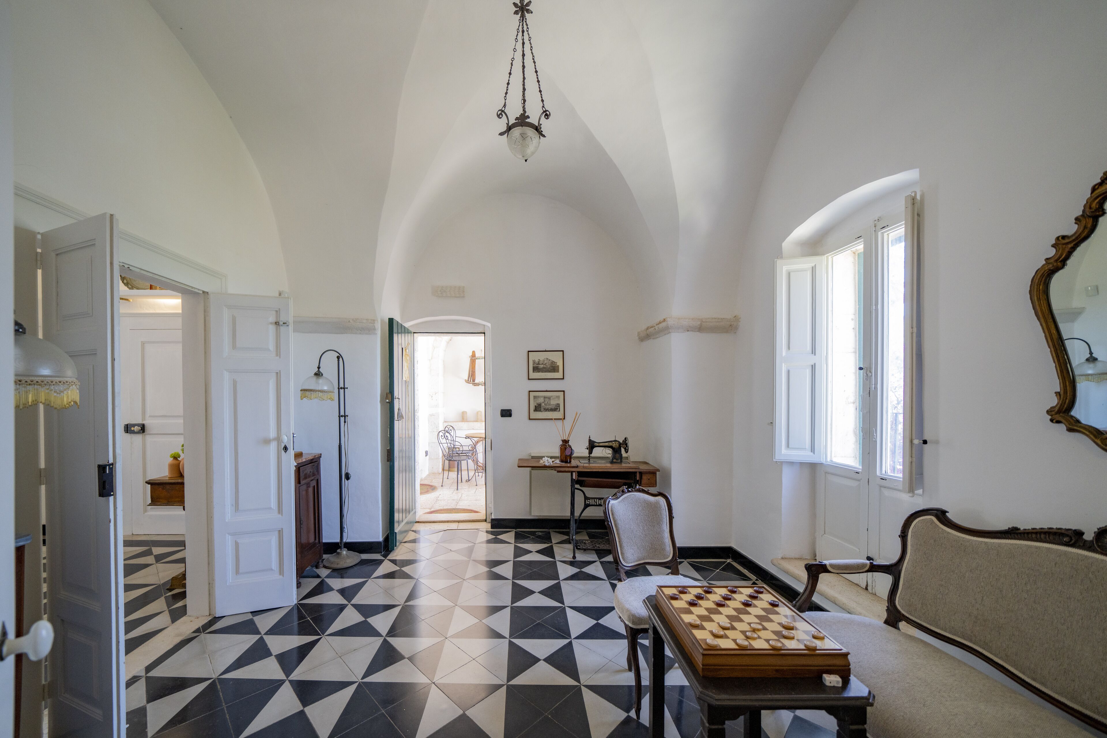 Une pièce avec un sol à carreaux, un jeu d’échecs, un canapé, une table et un miroir au mur.