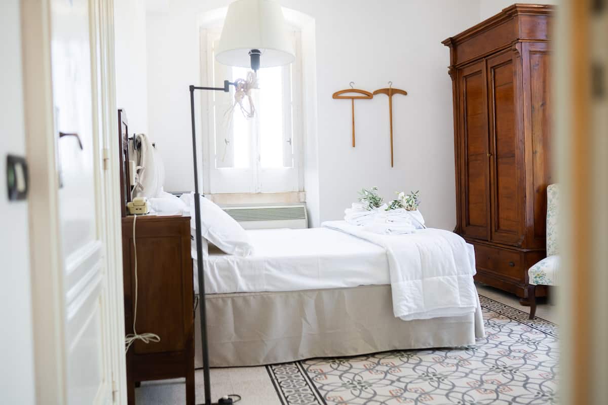 A bedroom with a bed, a wooden wardrobe, a hanging light fixture, and a patterned floor.