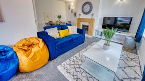 Un salon moderne avec un canapé bleu, des coussins jaunes et blancs, une table basse en verre et un téléviseur.