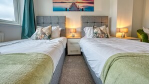 Une chambre d’hôtel avec deux lits, une table de chevet avec des lampes, un tableau représentant un coucher de soleil sur l’eau et une vue sur l’extérieur.