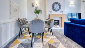 Un salon moderne avec un canapé bleu, un coin repas comprenant une table et des chaises, une cheminée et une horloge murale.