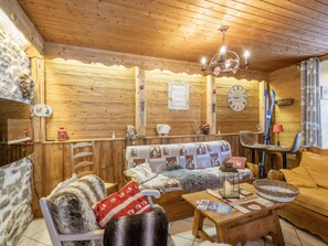 A cozy wooden interior with a sofa, chairs, a table, and a chandelier.