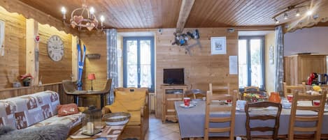 L’intérieur chaleureux d’un chalet avec un plafond en bois, un canapé, une table à manger et un téléviseur.