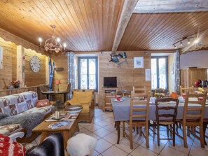 Ein gemütliches Blockhauss-Interieur mit Holzbalkendecke, einer Couch, einem Esstisch und einem Fernseher.