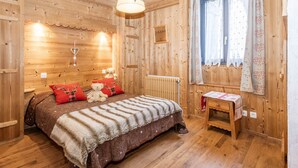 Et hyggeligt træhusværelse med en seng, et lille bord, et vindue med gardiner og en radiator.