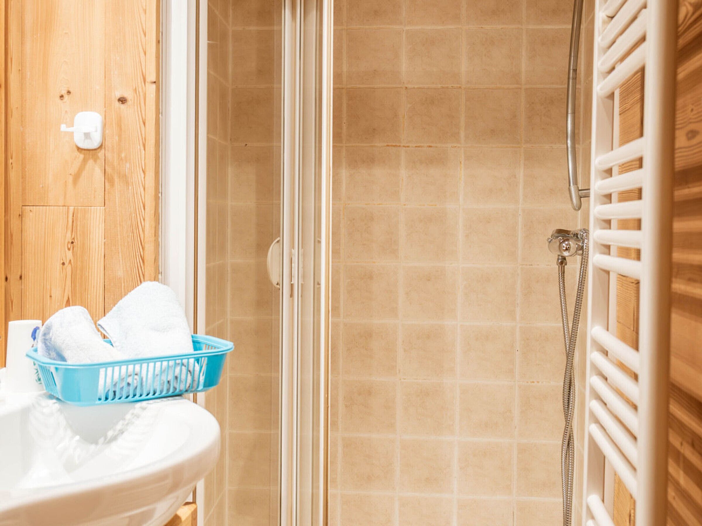 Une salle de bain avec une douche, un lavabo blanc, un panier bleu et un mur en bois.