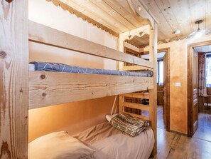 Ein Stockbett mit Kopfkissen und Decke, Holzwände und eine Tür zu einem anderen Raum.