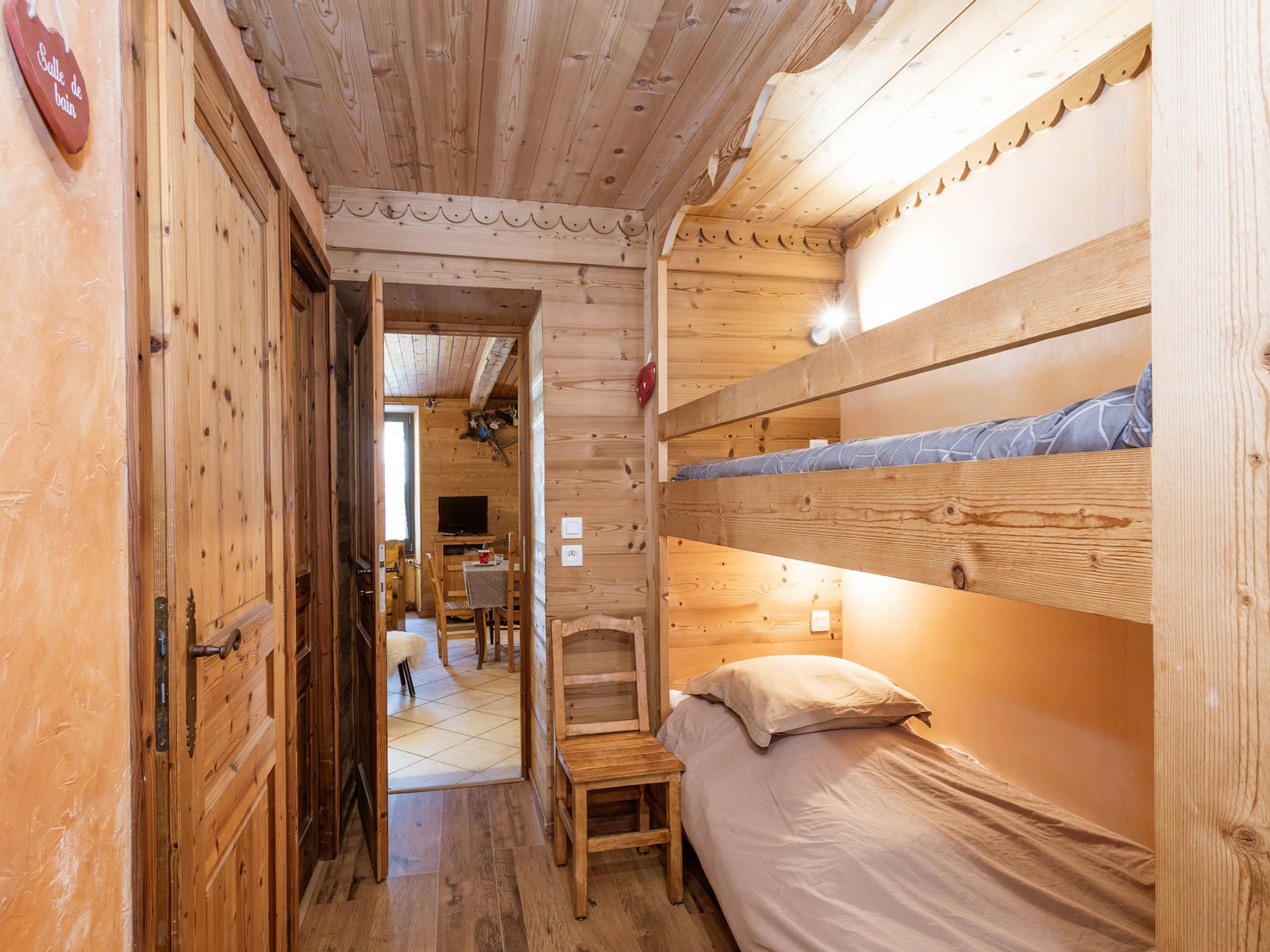 A wooden interior with a bunk bed, a small table, and a chair.