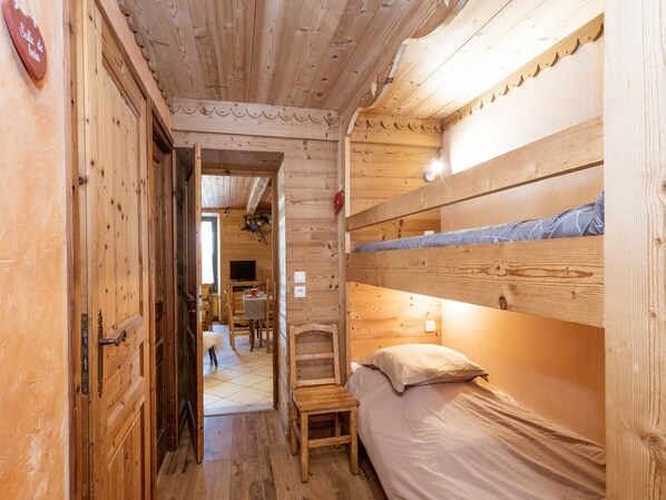 A wooden interior with a bunk bed, a small table, and a chair.