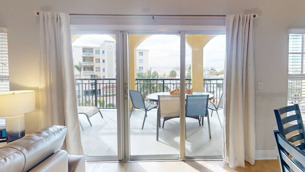 A balcony with a sliding glass door, a dining table with chairs, and a view of a residential building. - Beach Views, Steps to the Beach Access. Waterfront Resort Heated Pool & Hot Tub. Fishing Dock. (Treasure Island)