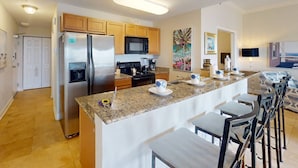 A modern kitchen with stainless steel appliances, a granite countertop, and a bar area with stools. - Beach Views, Steps to the Beach Access. Waterfront Resort Heated Pool & Hot Tub. Fishing Dock. (Treasure Island)