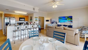 A modern kitchen with wooden cabinets, a central island, and a dining area with a round table and blue chairs. - Beach Views, Steps to the Beach Access. Waterfront Resort Heated Pool & Hot Tub. Fishing Dock. (Treasure Island)