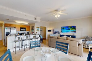 A modern kitchen with wooden cabinets, a central island, and a dining area with a round table and blue chairs.