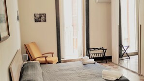 A bedroom with a bed, a chair, a desk with a lamp, a mirror, and a door with a view of the outside. - Residenza Diana (Syracuse)