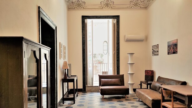 A room with a hexagonal patterned floor, a brown leather sofa, a wooden table, and a tall white vase. - Residenza Diana (Syracuse)