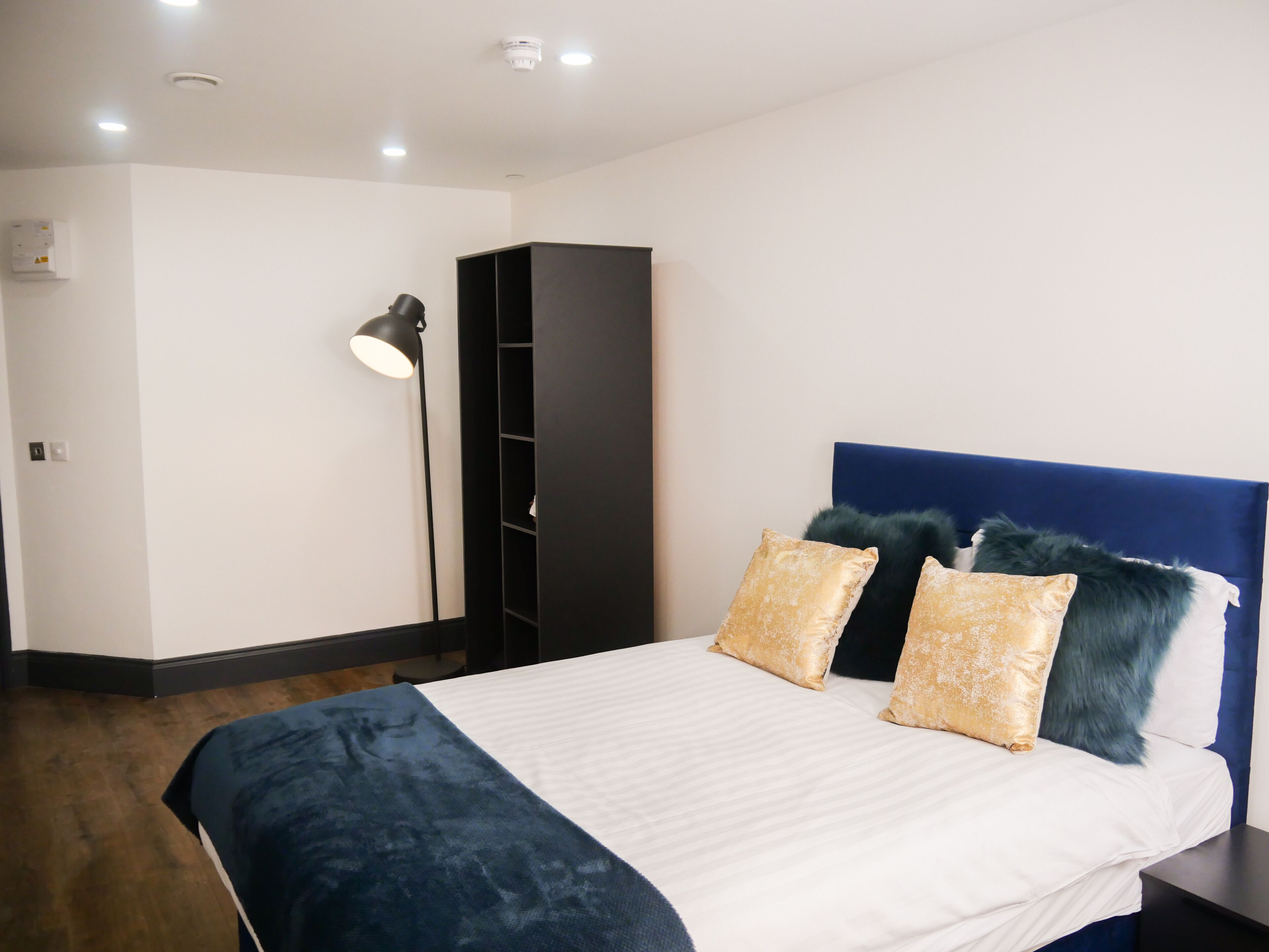 A bedroom with a bed, a wardrobe, a floor lamp, and a ceiling light.