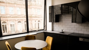 A modern kitchen with a round table and yellow chairs, a window with a view of a historic building, and a black cabinet with a TV above the sink. - New Oxford House Apartments (Liverpool)