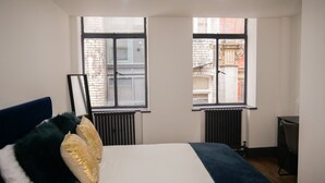 A bedroom with a bed, two windows, a radiator, and a desk. - New Oxford House Apartments (Liverpool)