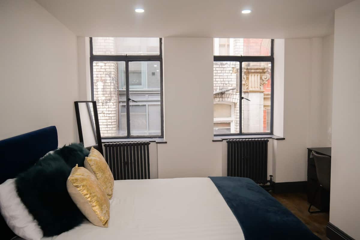 A bedroom with a bed, two windows, a radiator, and a desk.
