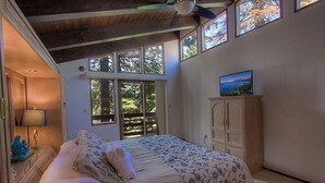Ein Schlafzimmer mit Bett, einem Fernseher auf einem Schrank und einem Fenster mit Blick auf Bäume.