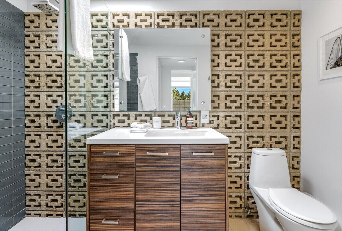 A bathroom with patterned tiles, a wooden vanity, a white sink, and a toilet.