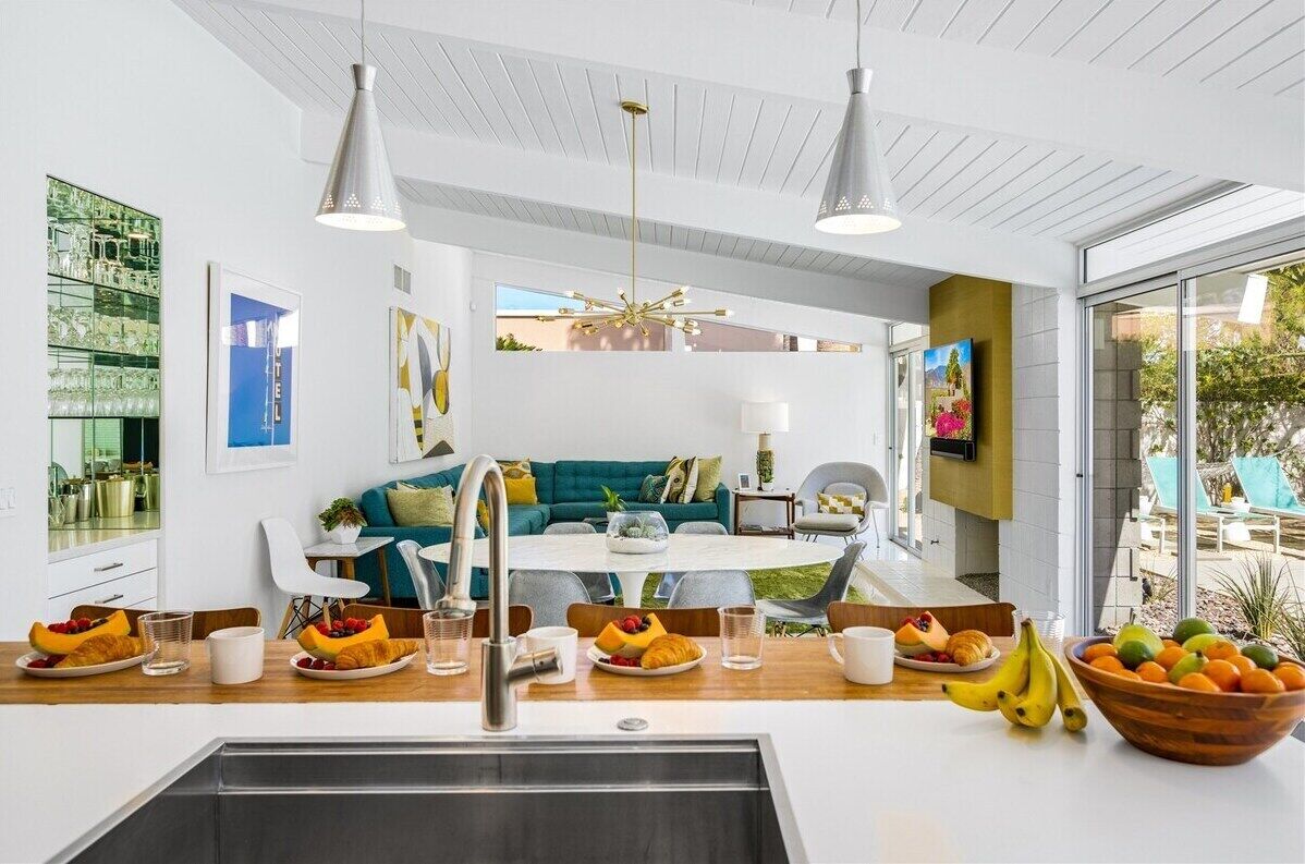 Cozinha moderna com ilha central, sala de jantar com mesa redonda e área de estar com sofá e cadeiras.
