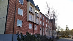 A multi-story brick building with balconies, a paved driveway, and sparse vegetation. - West Side Hotel (Turku)