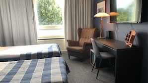 A hotel room with two beds, a desk, a chair, a lamp, and a TV. - West Side Hotel (Turku)