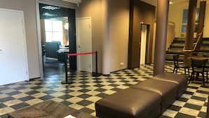 A lobby with a checkered floor, a brown leather sofa, a table with a magazine, and a staircase with chairs. - West Side Hotel (Turku)