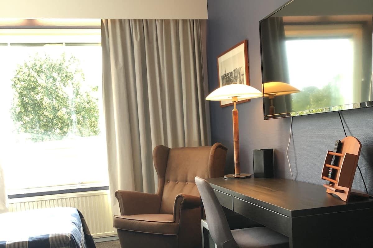 Ett hotellrum med en säng, ett skrivbord, en stol, en lampa och en tv.