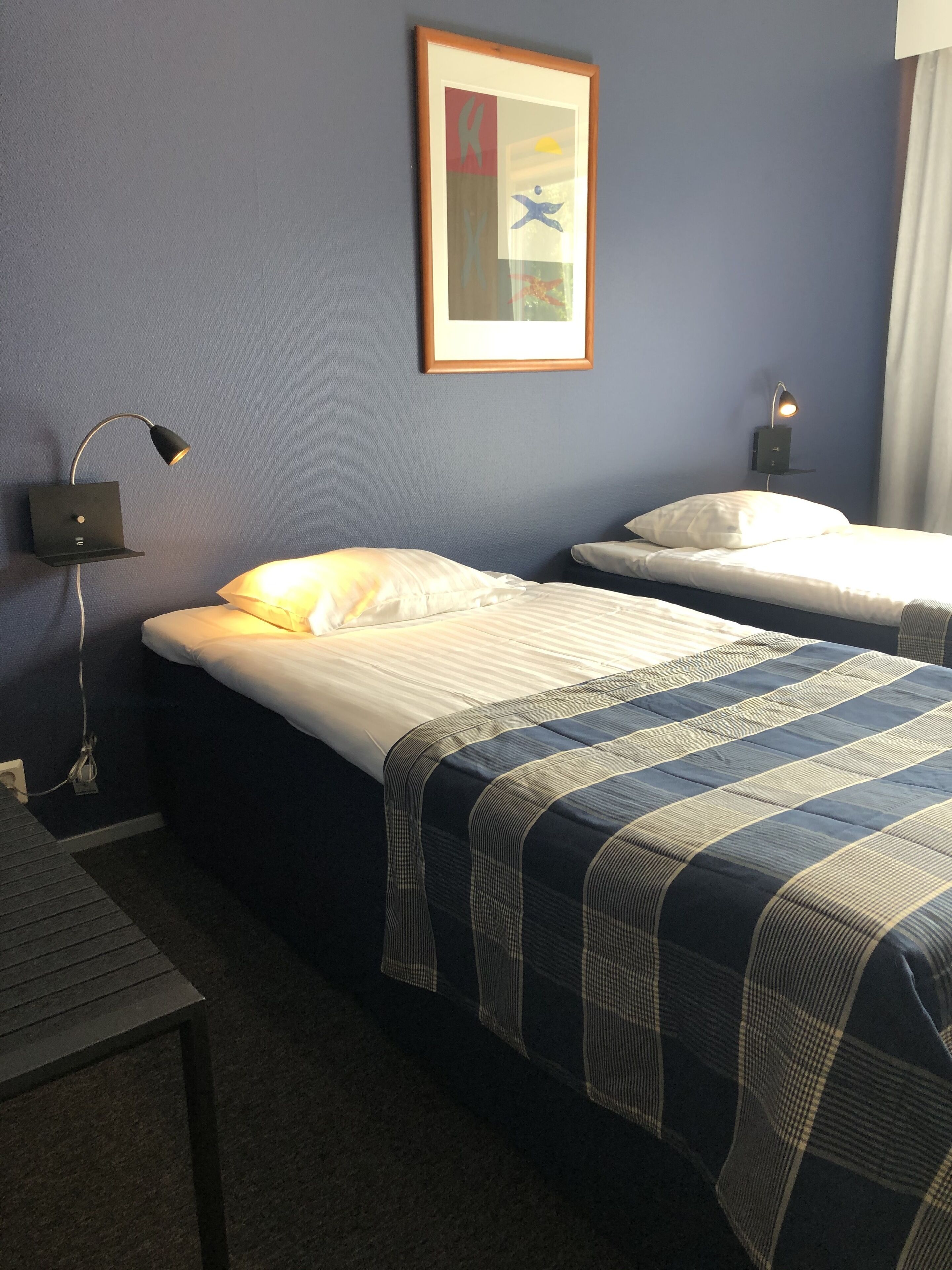 Habitació d'hotel amb dos llits, un escriptori, una obra d'art amb marc a la paret i una làmpada penjada a la pared.