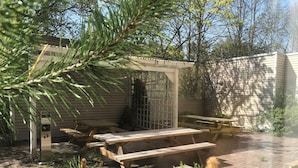An outdoor patio area with wooden picnic tables and benches, surrounded by a brick floor and greenery. - West Side Hotel (Turku)