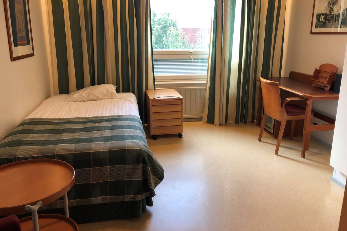 Ett sovrum med en säng, ett skrivbord, en stol, ett litet bord och ett element.