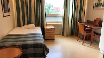 Un dormitorio con cama, escritorio, silla, una mesita y un radiador.
