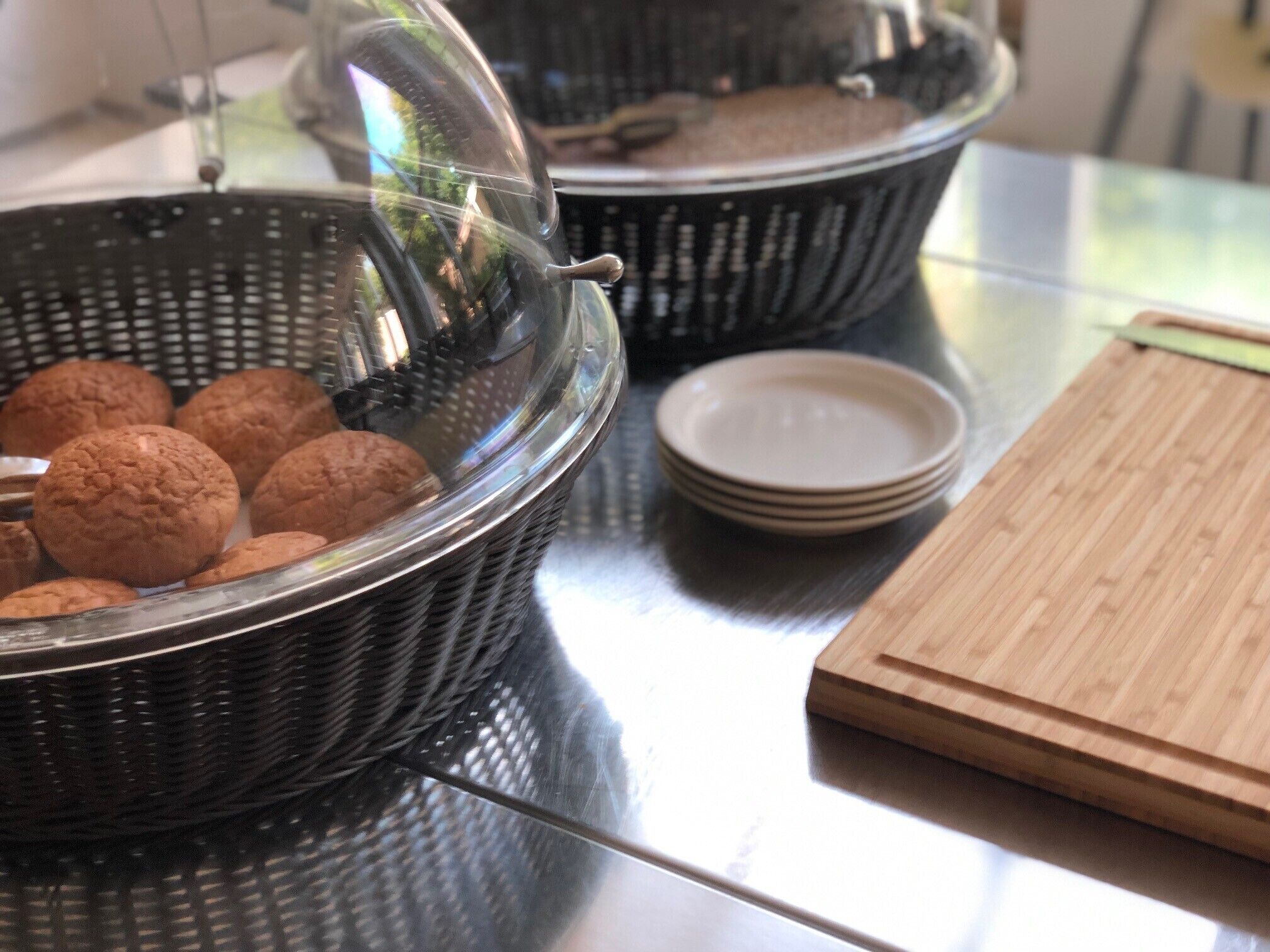 Una encimera de cocina con una cesta de galletas, una pila de platos y una tabla de cortar de madera.
