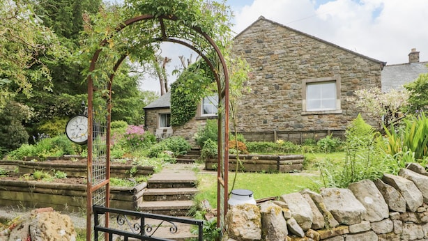 Una casa in pietra con un giardino, un cancello in metallo e un orologio.