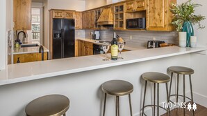 Eine moderne Küche mit Holzschränken, einem schwarzen Kühlschrank, einer Mikrowelle und einer Bar mit Hockern.