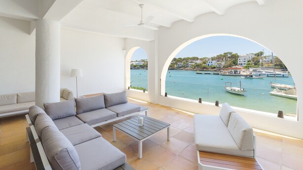 Un salón moderno con un sofá, sillones y una mesa de centro, con vistas a una marina llena de barcos y edificios.