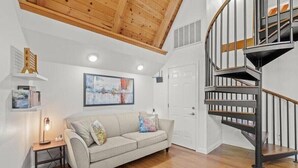 A living room with a wooden ceiling, a grey sofa, a small table with a lamp, a painting on the wall, and a spiral staircase. - Alexander Valley Russian River Home for 8, Spa, WiFi, BBQ, bocce, vineyard (Cloverdale)